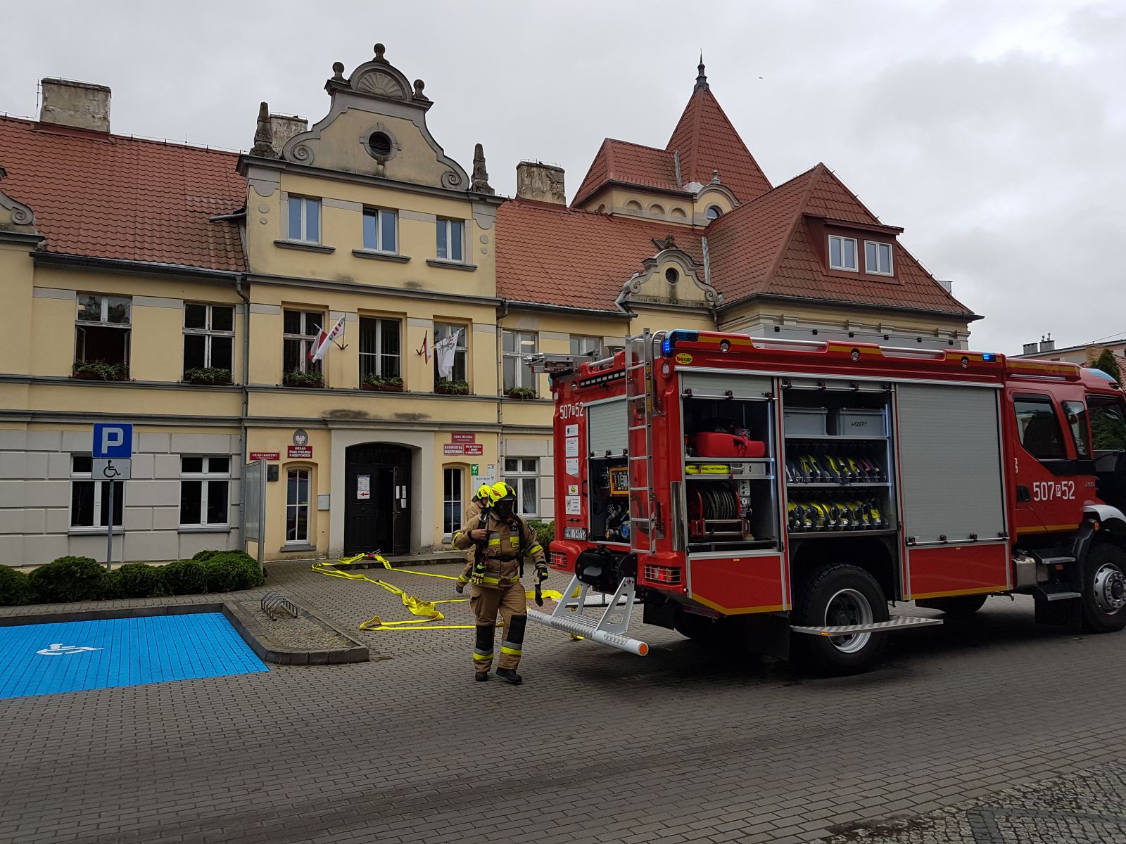Zdjęcie przedstawia urząd miasta, wóz strażacki oraz strażaka