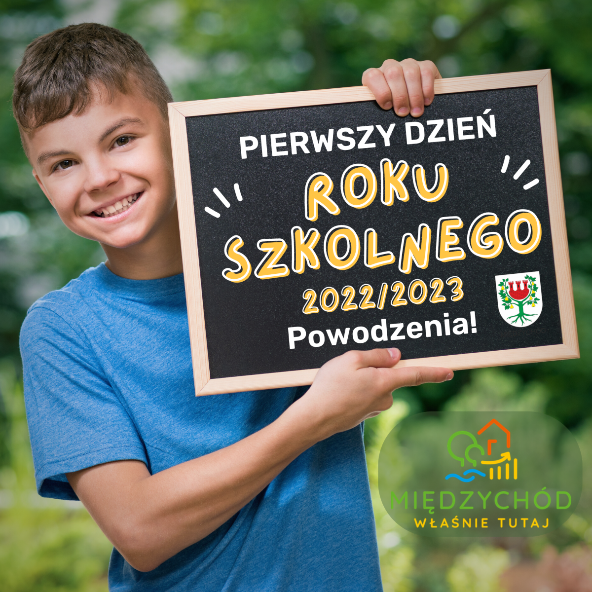 Uśmiechnięty chłopiec trzyma w rękach tablicę z życzeniami powodzenia w roku szkolnym 2022/2023
