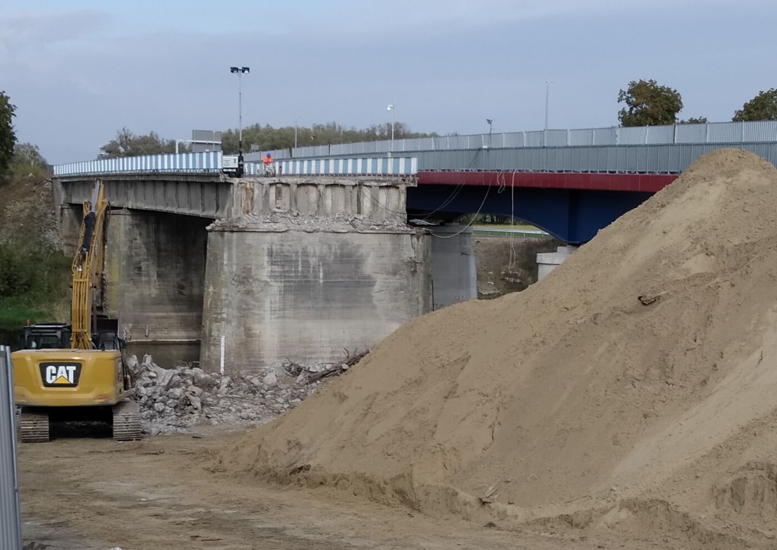 Zdjęcie przedstawia roboty rozbiórkowe. Widać na nim koparkę  oraz most
