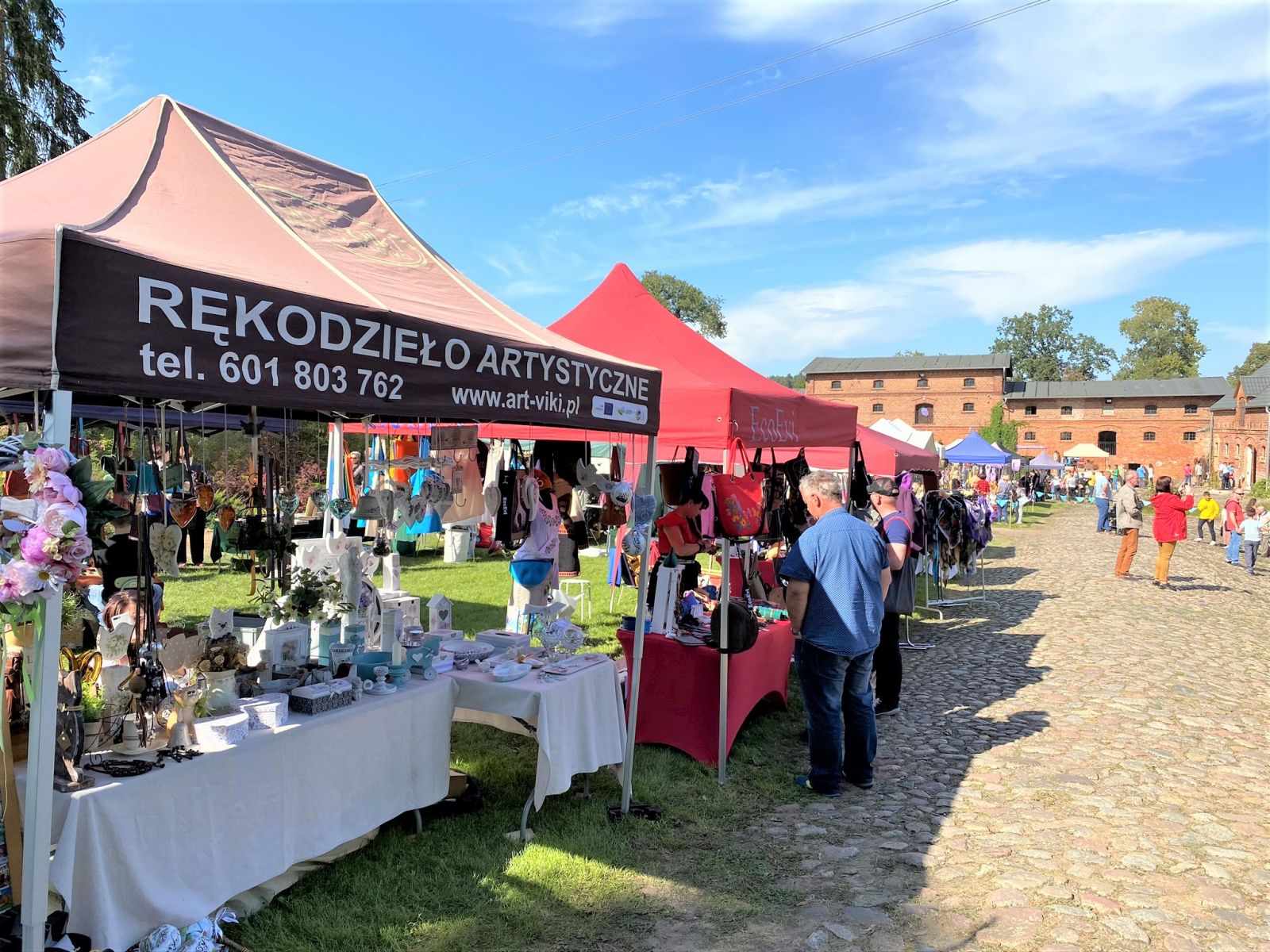 Zdjęcie przedstawia stoiska podczas XIV Smażenie Powideł w Mniszkach. Można na nich zobaczyć rękodzieła oraz namioty