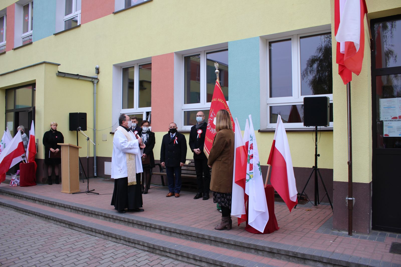 Zdjęcie przedstawia ludzi, którzy biorą udział w uroczystości nadania imienia szkole. 