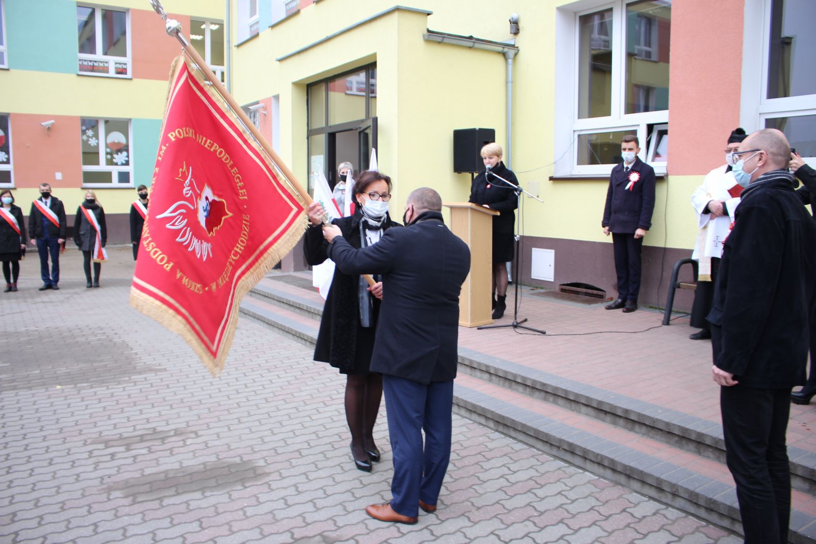 Zdjęcie przedstawia ludzi, którzy biorą udział w uroczystości nadania imienia szkole. 